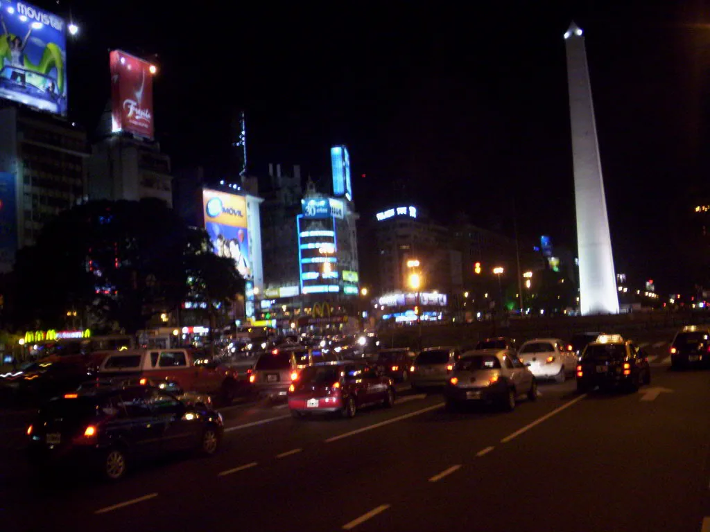The Obelisco de Buenos Aires and Avenida 9 de Julio lit up at night, with traffic and illuminated billboards